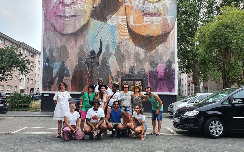 Group of people standing in front of a large painted mural on a wall.