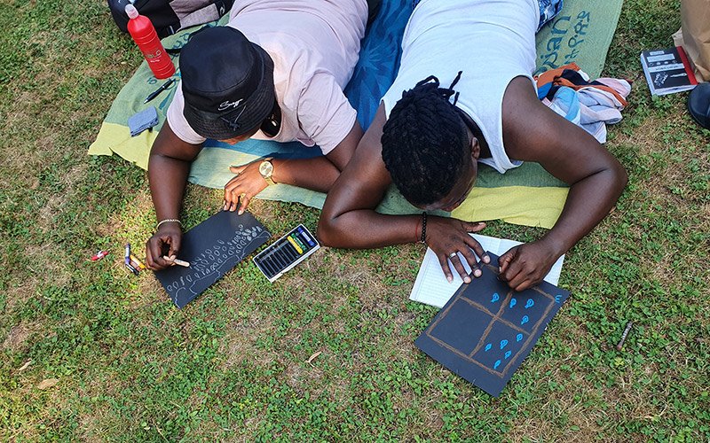 2 people lying on a grassy lawn drawing.